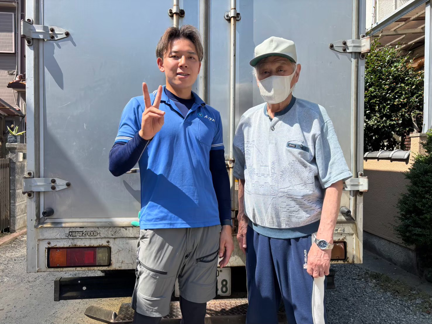 泉佐野市で不用品回収を完了しトラックの前でお客様と笑顔で並ぶイーブイの作業スタッフ